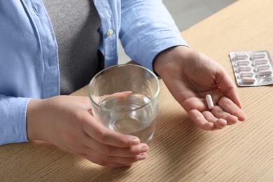 Photo of Woman with glass of water and pill at wooden table, closeup