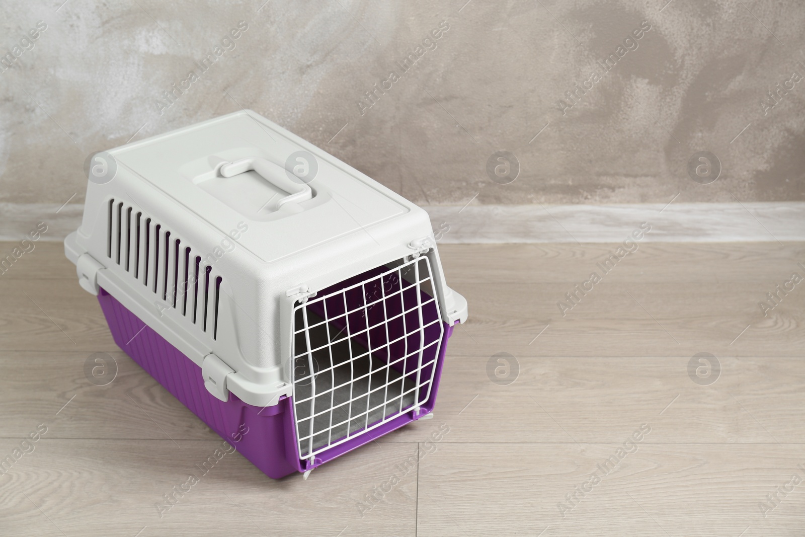 Photo of Violet pet carrier on floor near beige wall, space for text