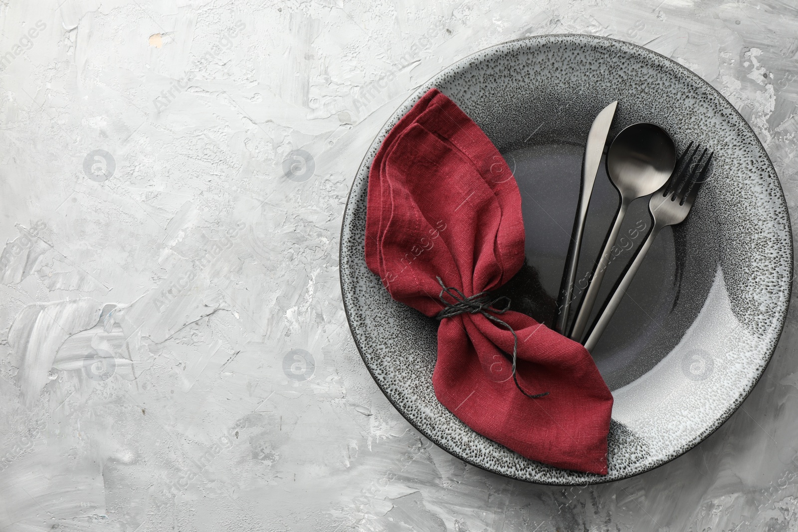 Photo of Stylish setting with cutlery, napkin and plate on grey textured table, top view. Space for text