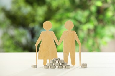 Pension savings. Figure of senior couple and coins on white table against blurred green background