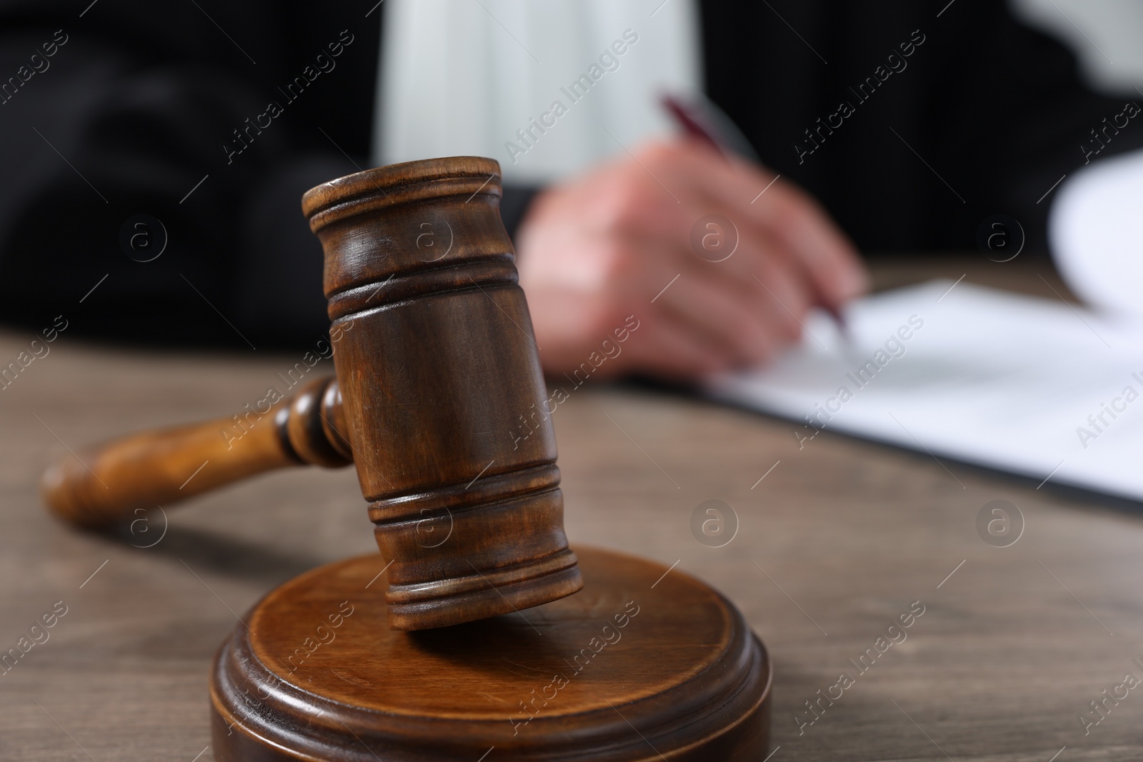 Photo of Judge with gavel writing in papers at wooden table, closeup