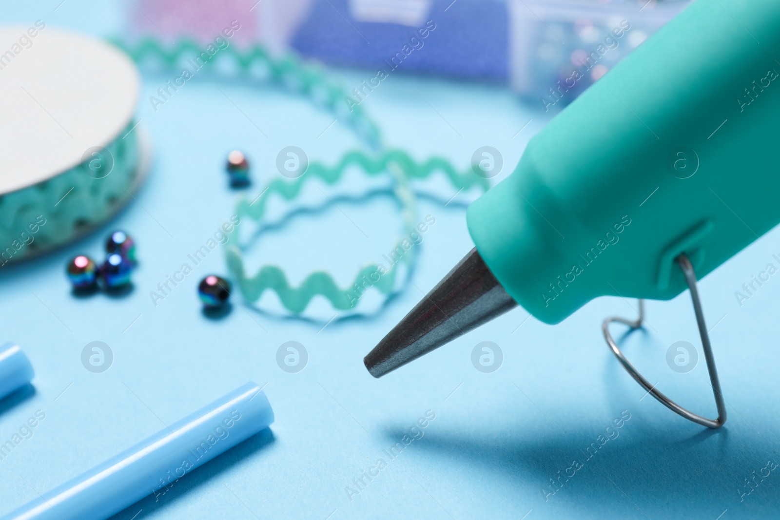 Photo of Hot glue gun and handicraft materials on light blue table, closeup