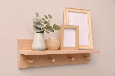 Wooden shelf with photo frames, candle and eucalyptus on beige wall. Interior element