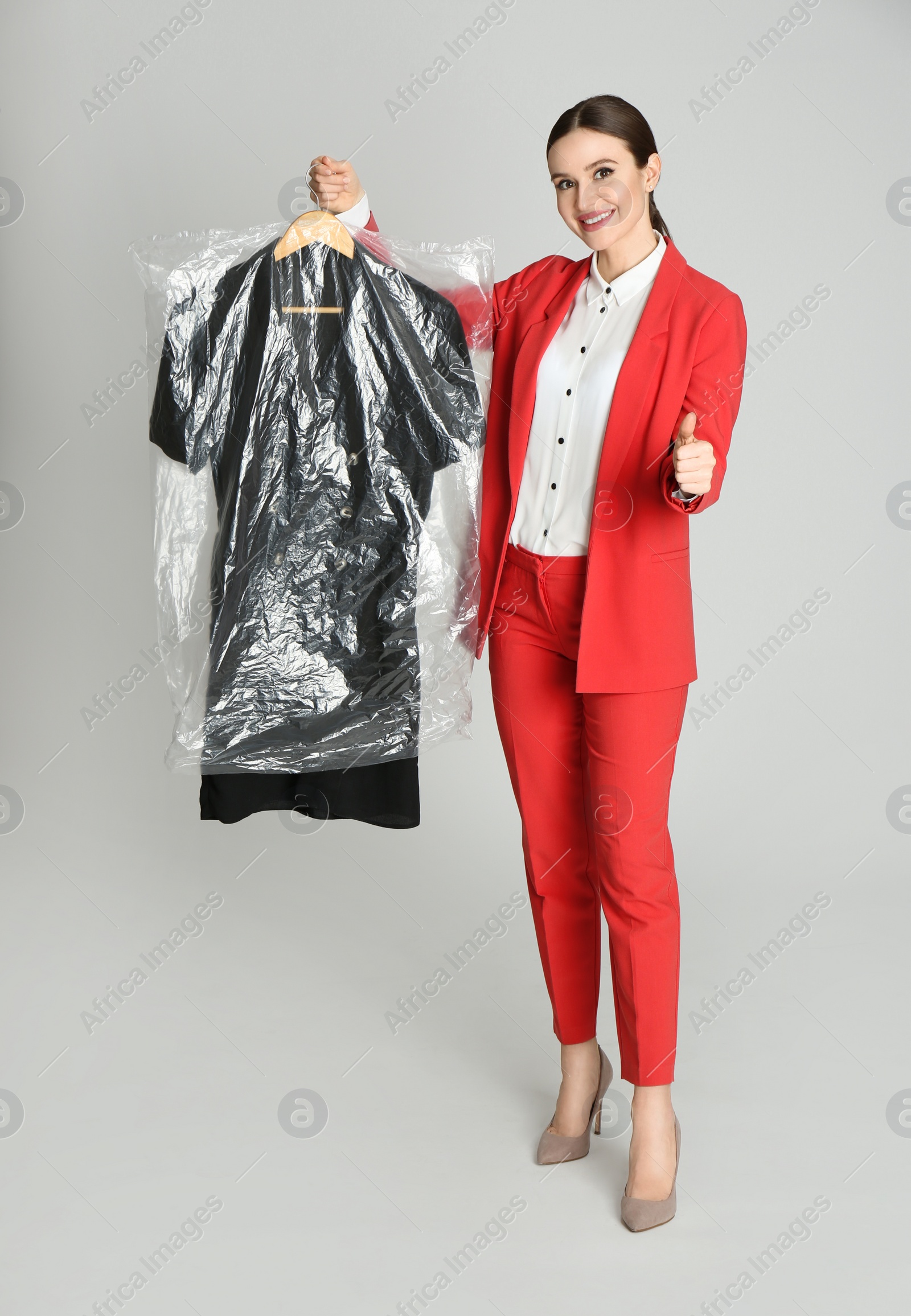Photo of Young woman holding hanger with dress on light grey background. Dry-cleaning service