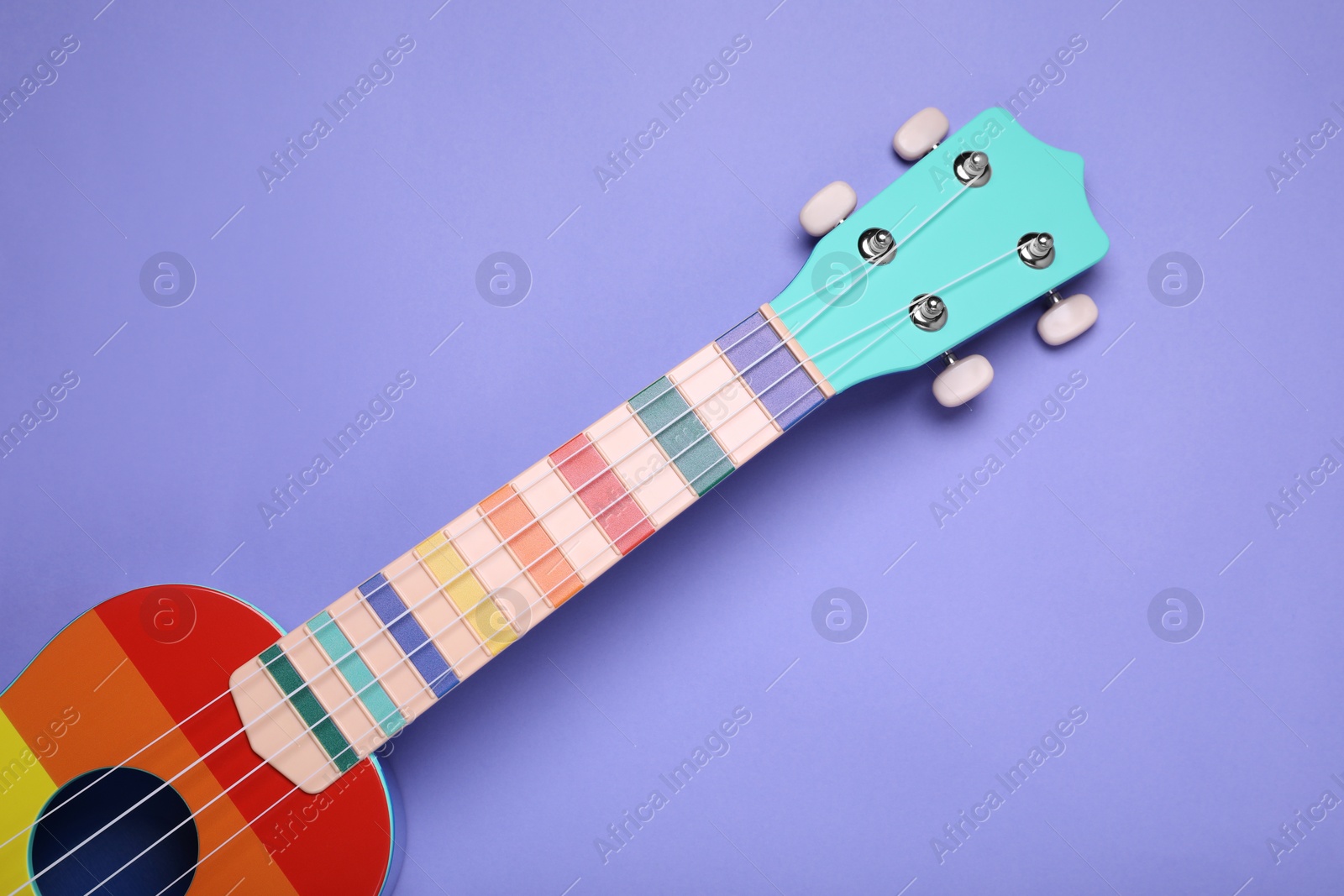 Photo of Colorful ukulele on purple background, top view. String musical instrument