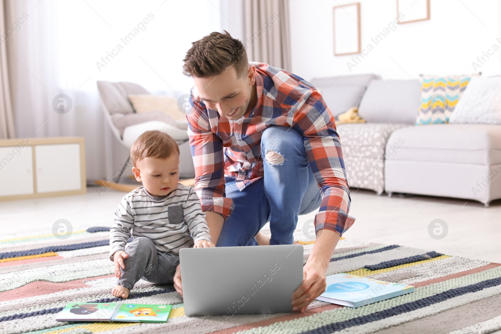 Photo of Young father with his cute little son using laptop at home