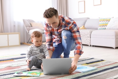 Young father with his cute little son using laptop at home