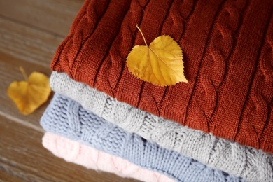 Photo of Stack of warm knitted clothes and autumn leaves on wooden background, above view