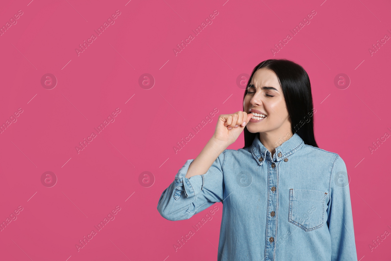 Photo of Young woman biting her nails on pink background. Space for text