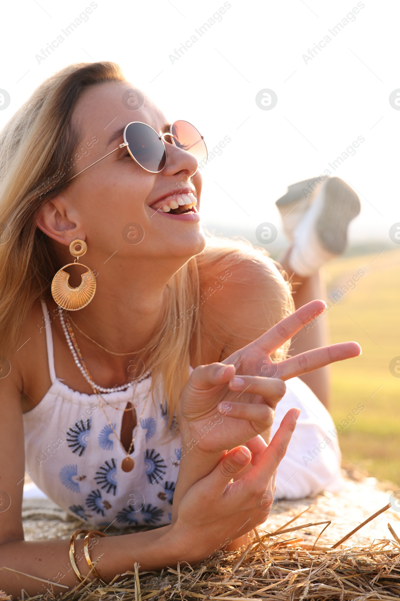 Photo of Beautiful hippie woman showing peace sign on hay bale in field