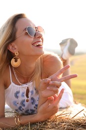 Photo of Beautiful hippie woman showing peace sign on hay bale in field