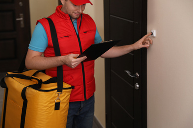Male courier with thermo bag and clipboard ringing doorbell. Food delivery service