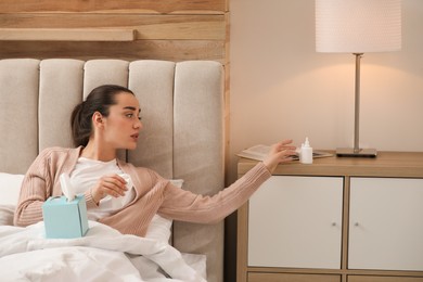 Photo of Sick young woman with napkins and nasal spray in bed at home