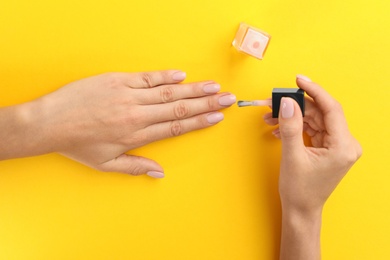 Woman applying nail polish on color background, above view