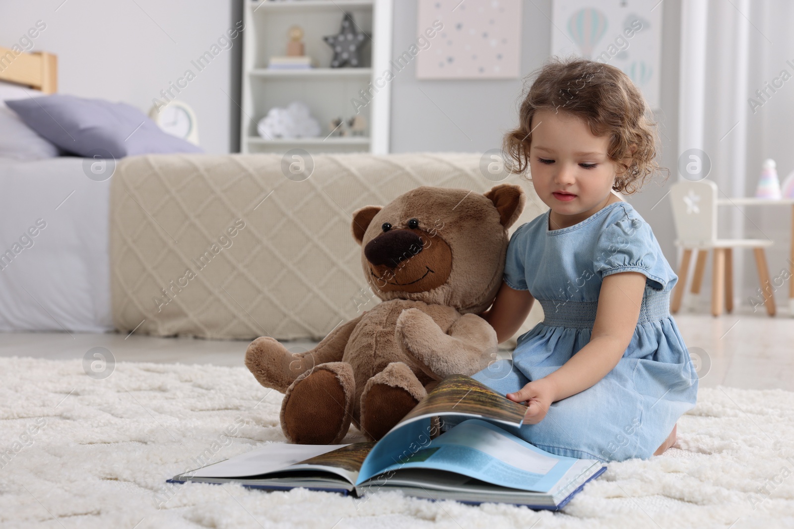 Photo of Cute little girl with teddy bear and book on floor at home