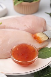 Photo of Marinade, basting brush and raw chicken fillets on table, closeup