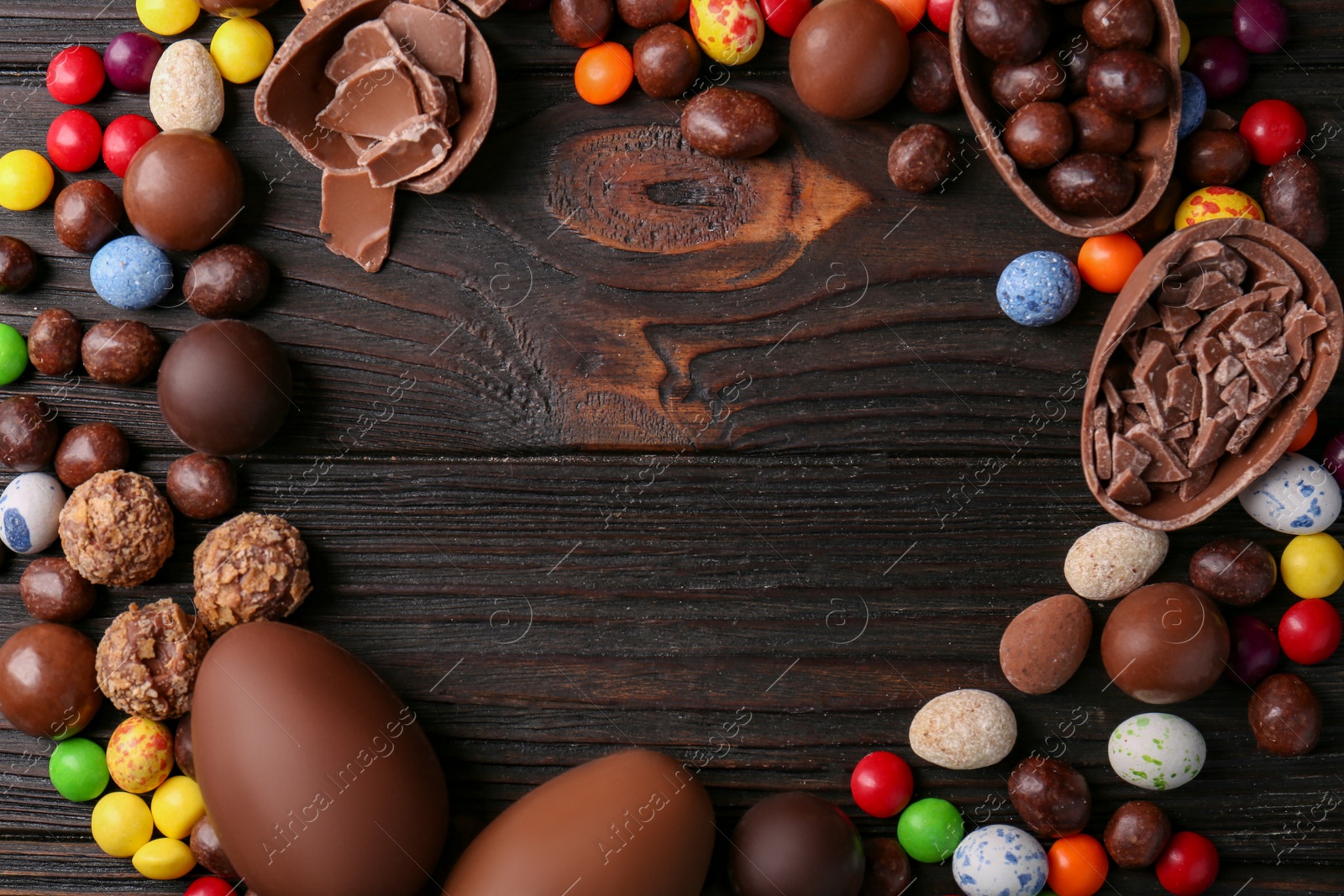 Photo of Frame made of tasty chocolate eggs and sweets on wooden table, flat lay. Space for text