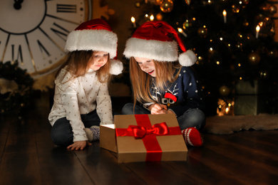 Cute children opening magic gift box near Christmas tree at night