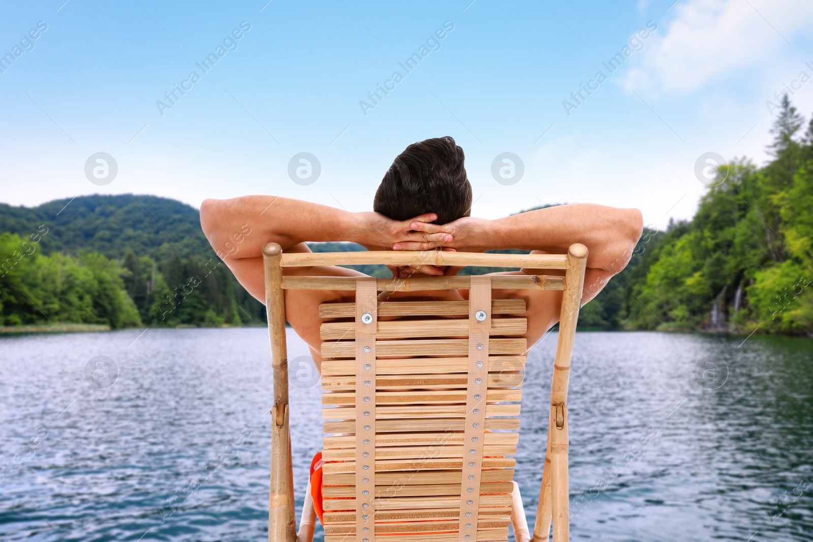 Image of Young man relaxing on sun lounger near river and mountains. Luxury vacation 