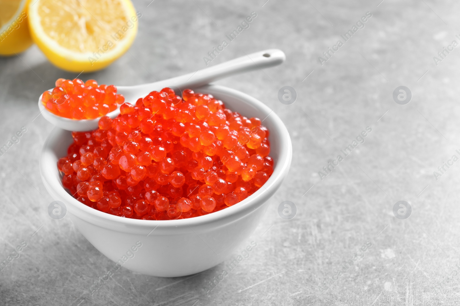 Photo of Ceramic bowl and spoon with delicious red caviar on table