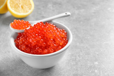 Photo of Ceramic bowl and spoon with delicious red caviar on table