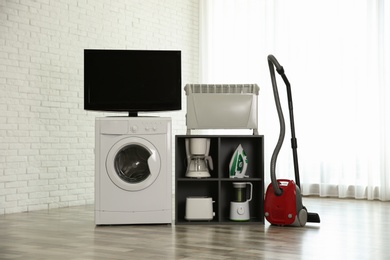 Photo of Modern vacuum cleaner and different household appliances near window indoors