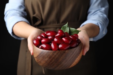 Woman with wooden bowl of fresh ripe dogwood berries on black background, closeup