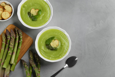 Photo of Delicious asparagus soup served on grey table, flat lay. Space for text