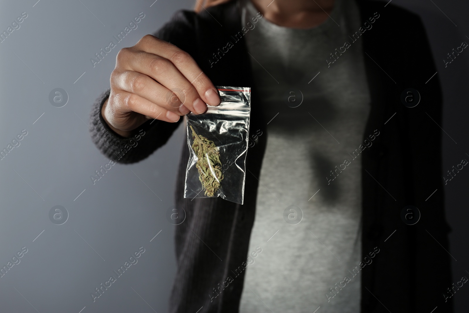 Photo of Female dealer holding hemp in plastic bag on color background, closeup