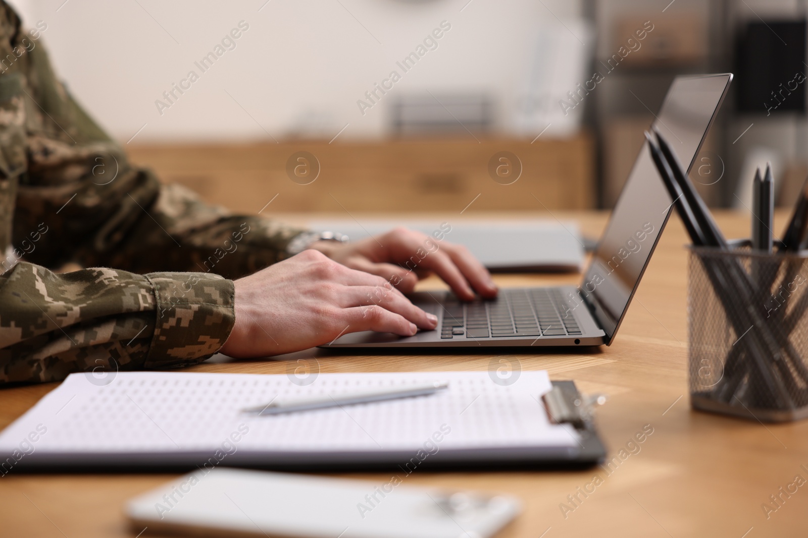 Photo of Military service. Soldier working with laptop at wooden table indoors, closeup