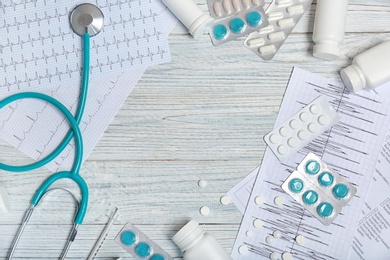 Photo of Flat lay composition with stethoscope and pills on wooden background. Cardiology service