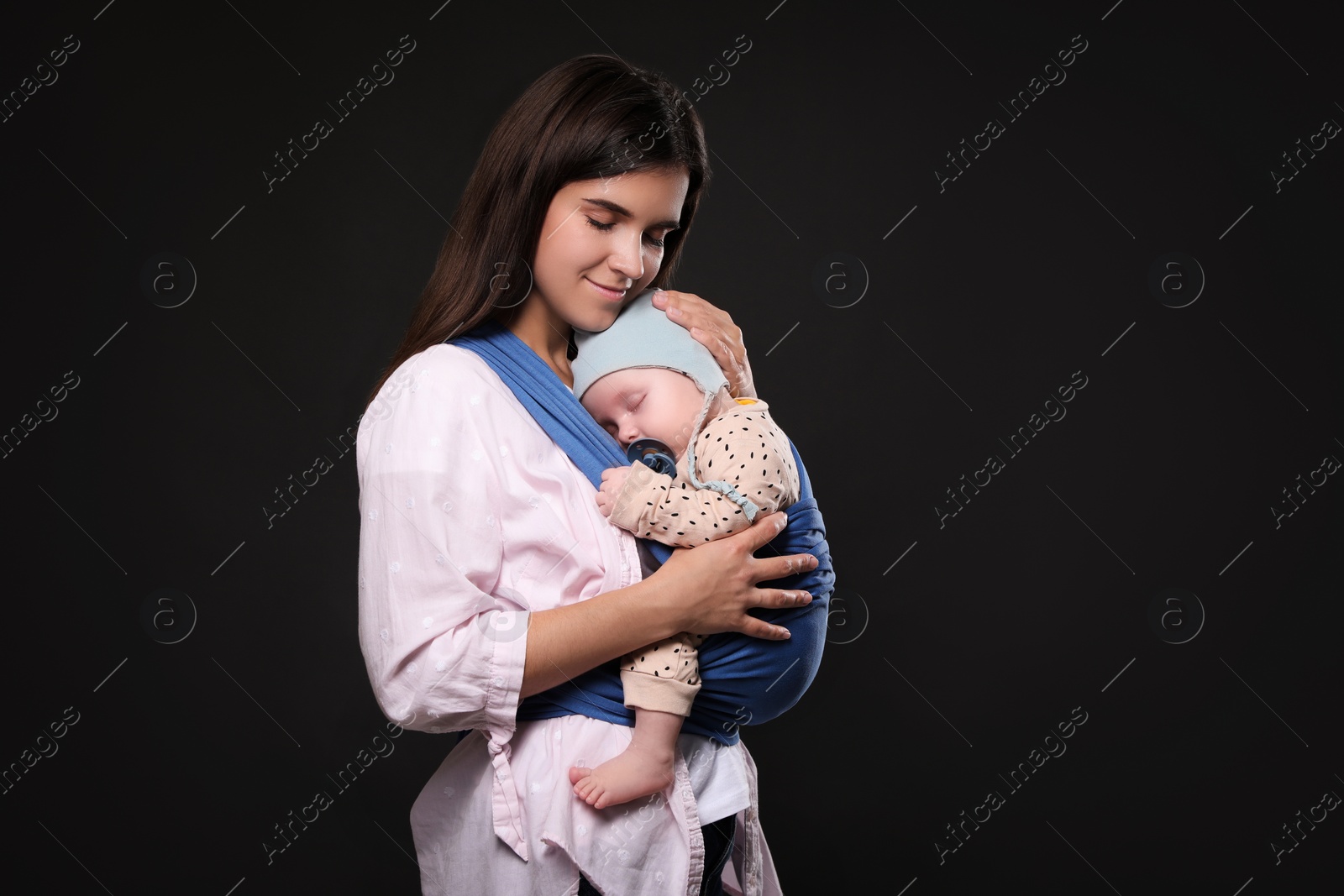 Photo of Mother holding her child in sling (baby carrier) on black background. Space for text