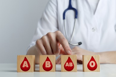 Image of Wooden cubes with images of drops representing different blood types and doctor at table, closeup