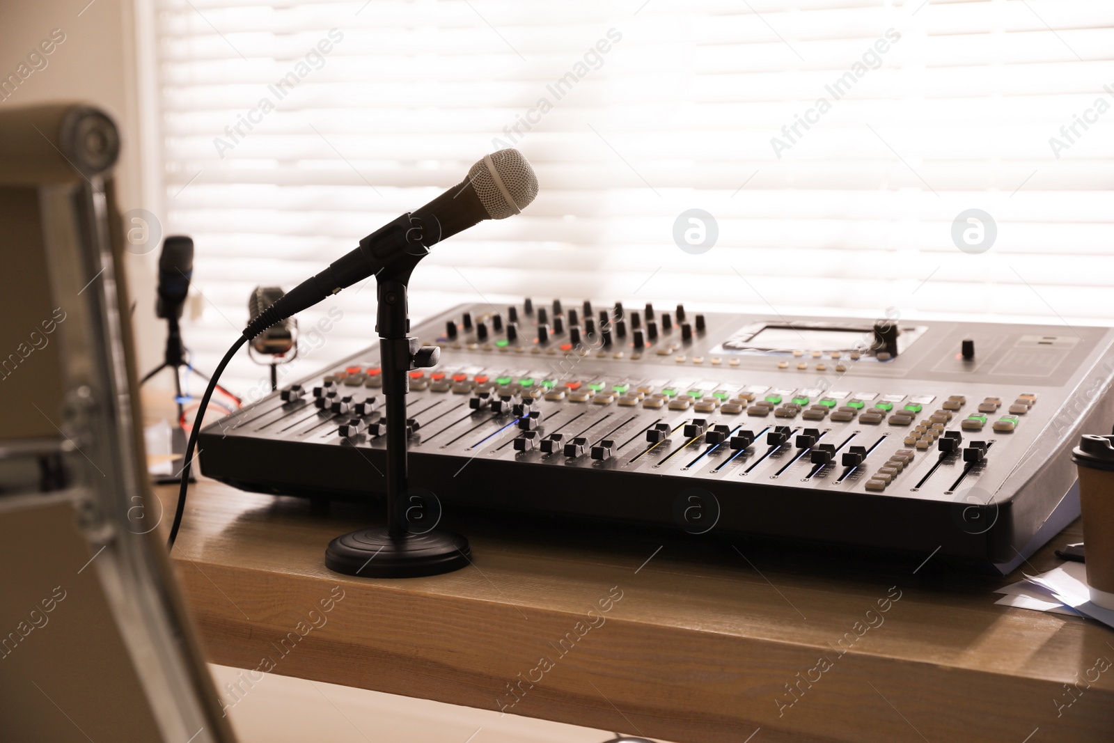 Photo of Microphone and professional mixing console on wooden table in radio studio