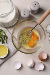 Photo of Flat lay composition with raw eggs and whisk in bowl on light table