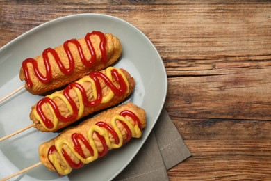 Delicious corn dogs with mustard and ketchup on wooden table, top view
