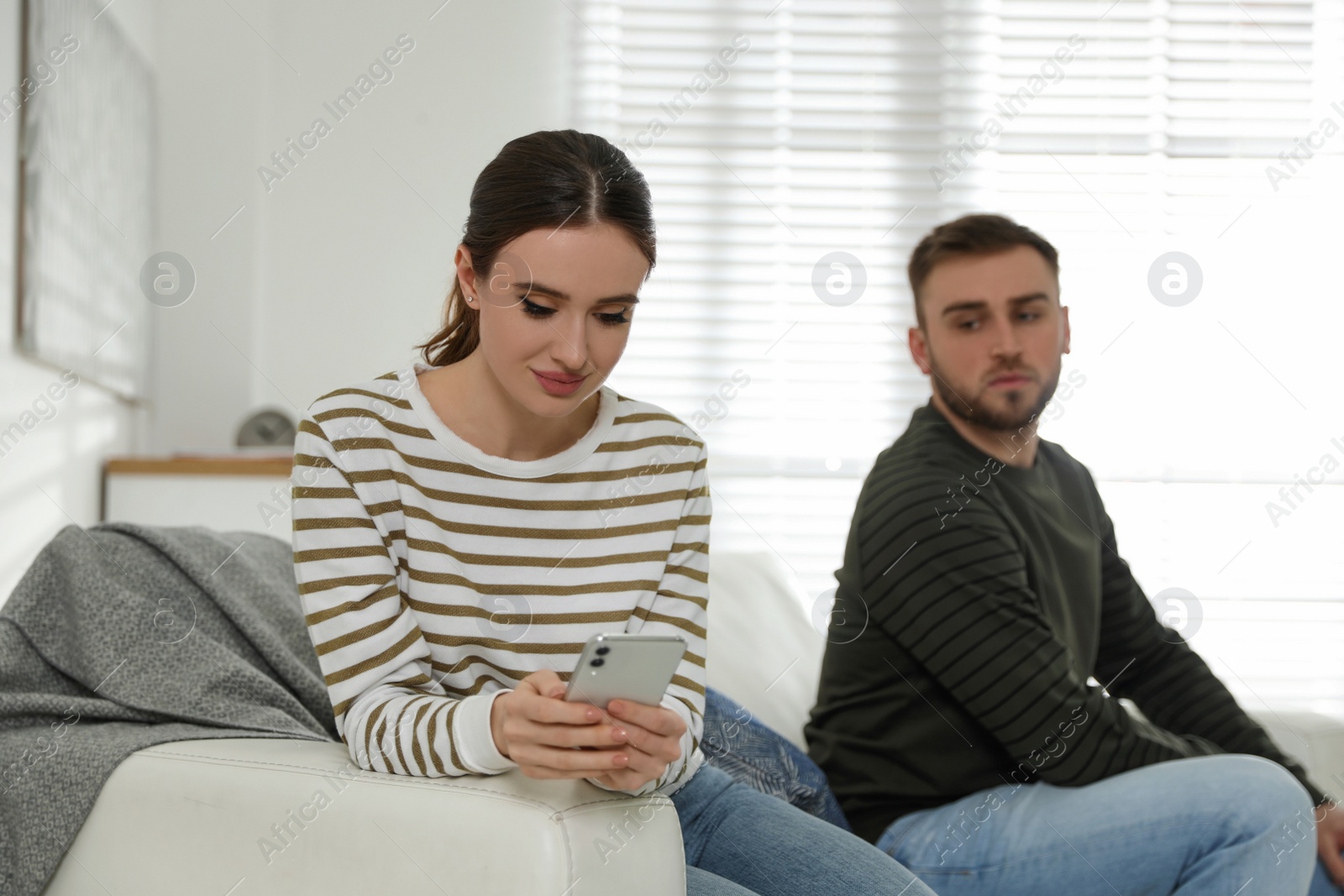 Photo of Young man peering into girlfriend's smartphone at home. Jealousy in relationship