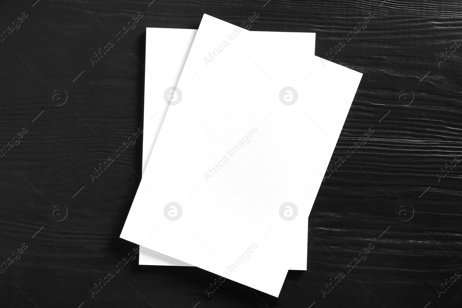 Photo of Stack of blank paper sheets for brochure on black wooden background, top view. Mock up