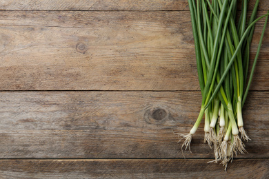 Photo of Fresh green spring onions on wooden table, flat lay. Space for text