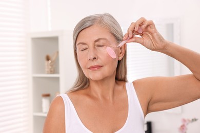 Photo of Woman massaging her face with rose quartz roller in bathroom