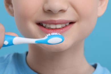 Photo of Girl brushing her teeth with toothbrush on light blue background, closeup