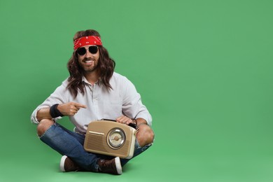 Photo of Stylish hippie man with retro radio receiver pointing at something on green background, space for text