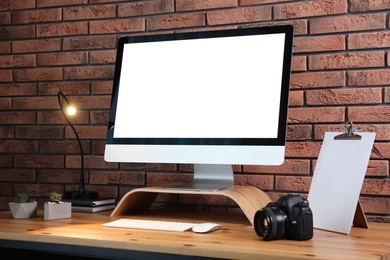 Photo of Comfortable workplace with modern computer on wooden table near brick wall. Space for text