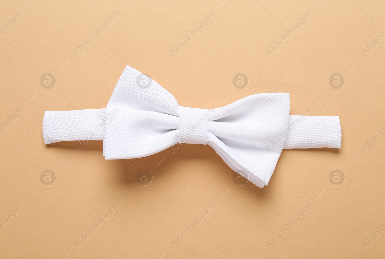 Photo of Stylish white bow tie on beige background, top view