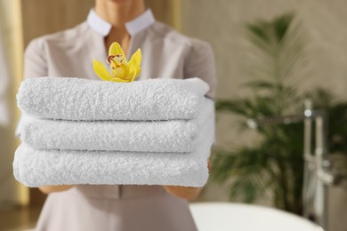 Photo of Chambermaid holding fresh towels with flower in hotel bathroom, closeup