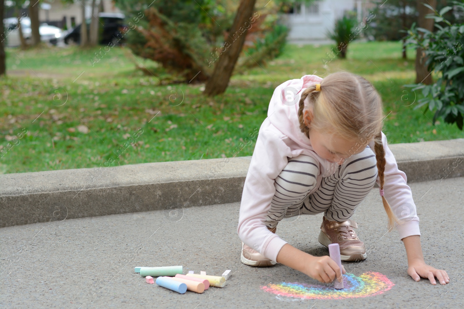 Photo of Little child drawing rainbow with chalk on asphalt