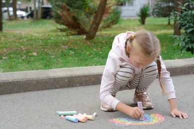 Photo of Little child drawing rainbow with chalk on asphalt