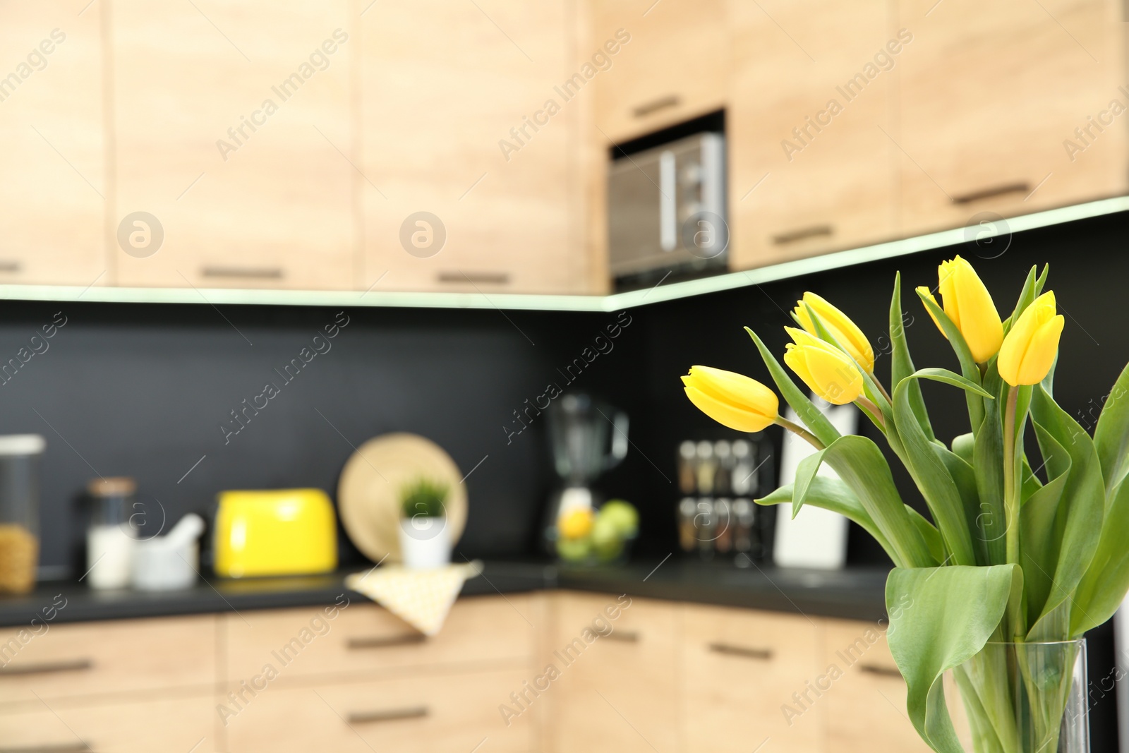 Photo of Beautiful tulips and blurred view of kitchen interior on background