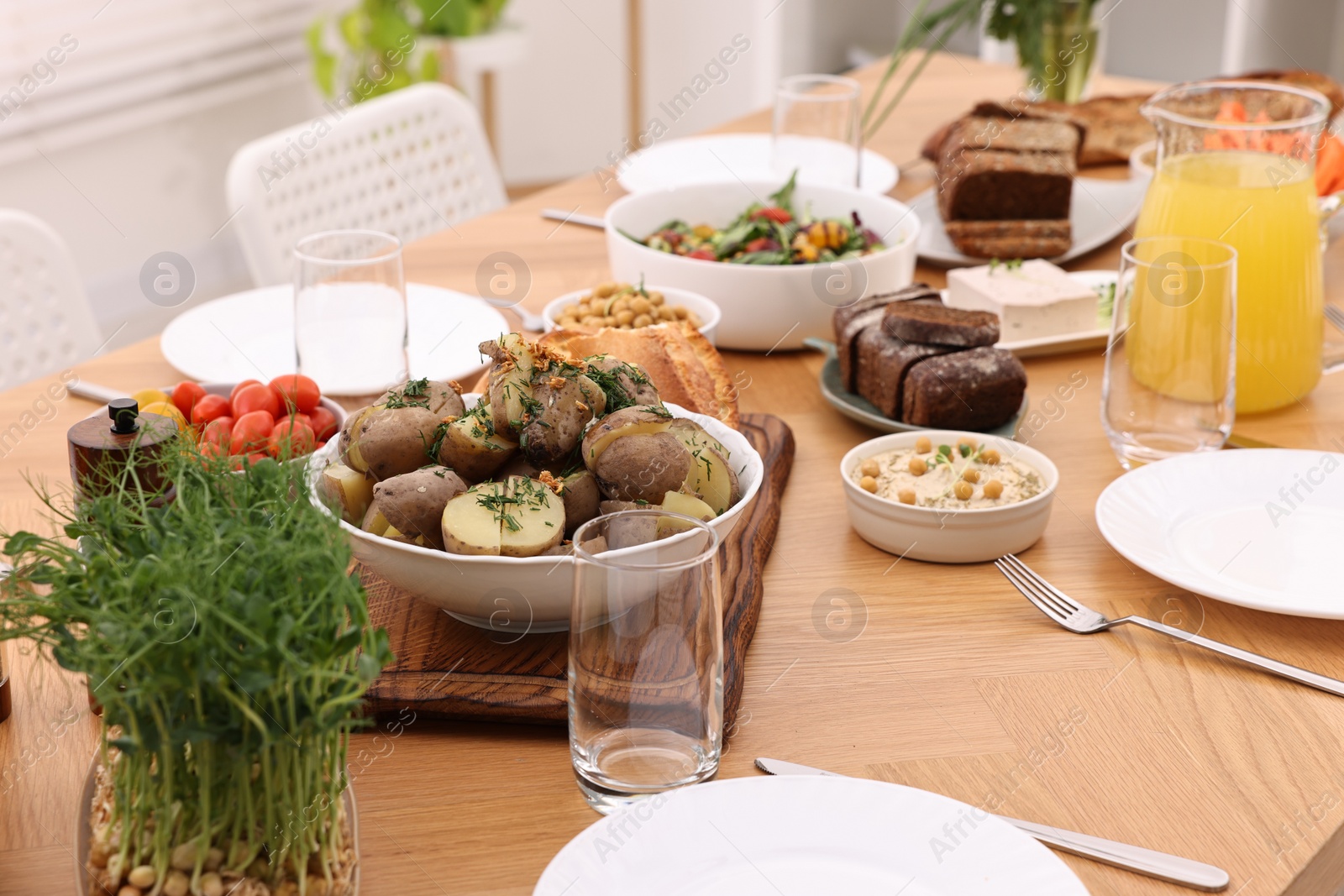 Photo of Healthy vegetarian food, jug of juice, cutlery, glasses and plates on wooden table indoors