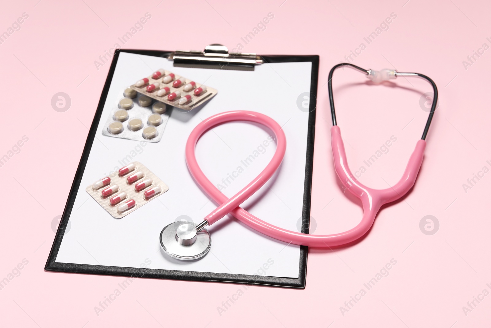 Photo of Stethoscope, clipboard and pills on pink background. Medical tool